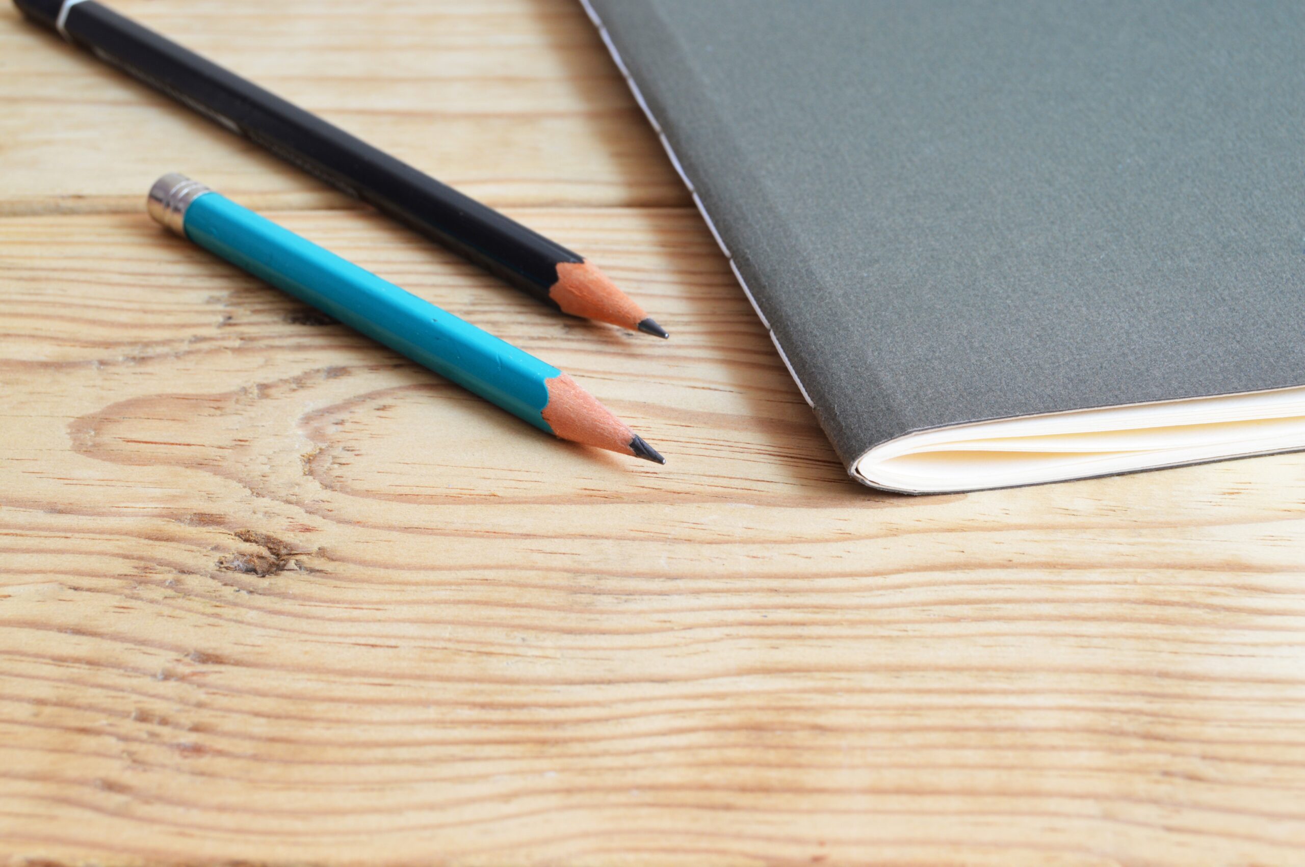 Black notebook with 2 pencils on wooden surface