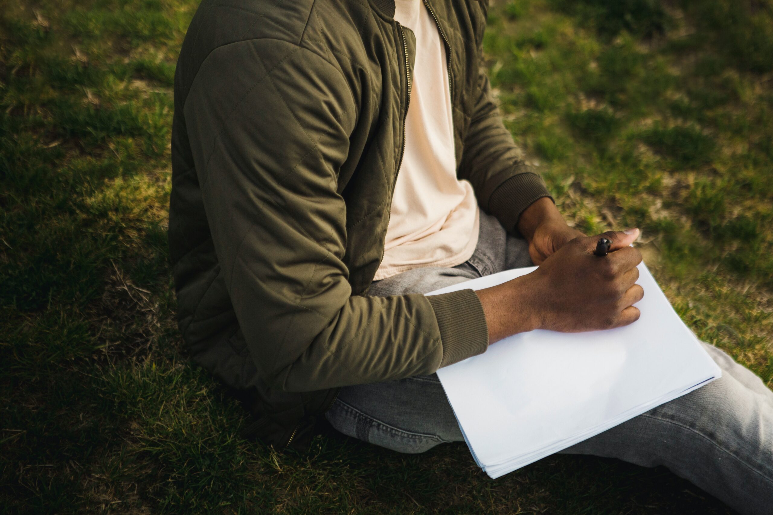 Person sitting on grass writing on paper