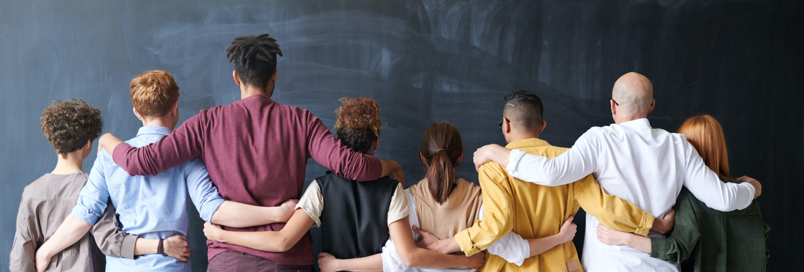 People facing a chalkboard with arms around each other's shoulders