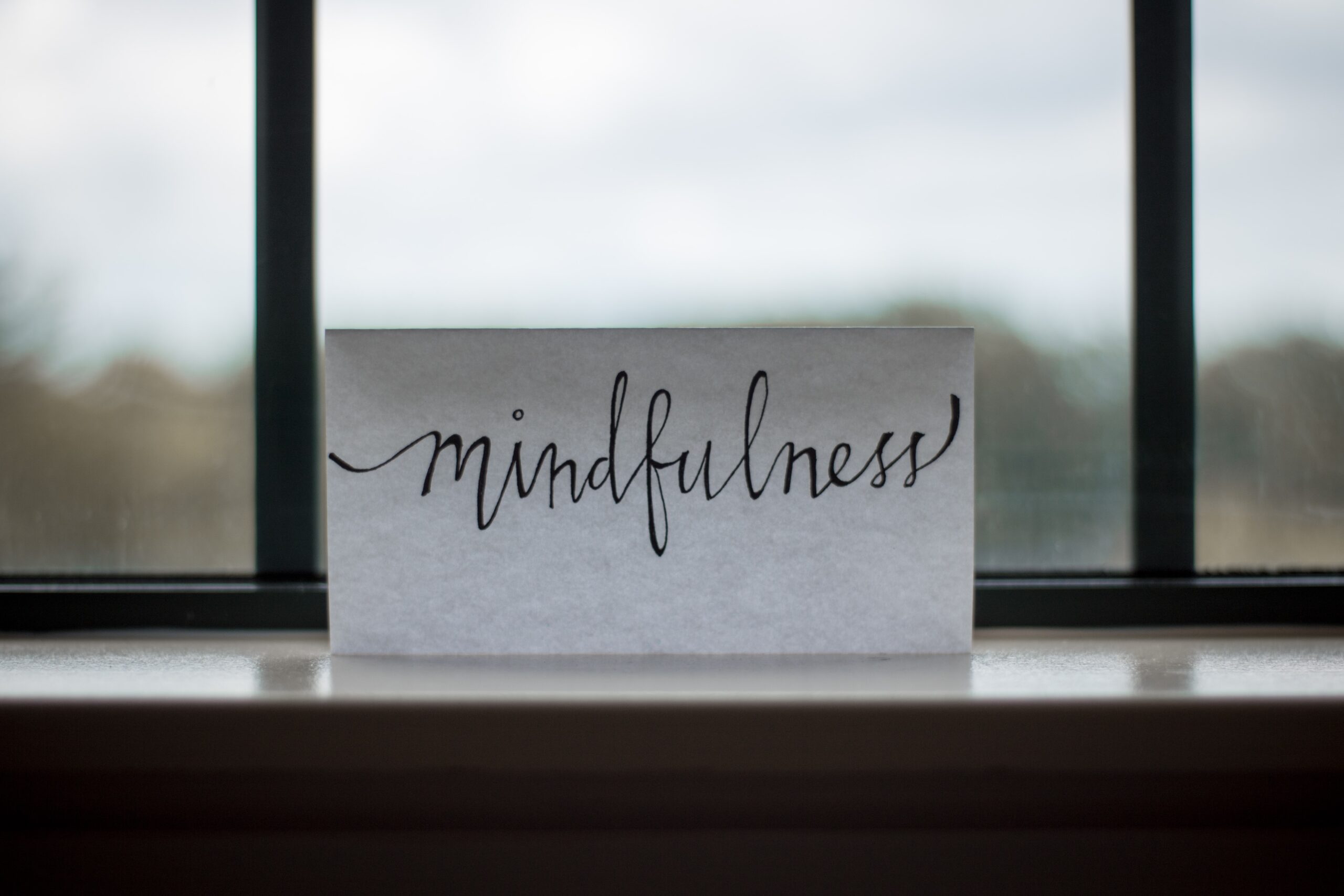 a white piece of paper propped up in a window with the word mindfulness hand written neatly on it